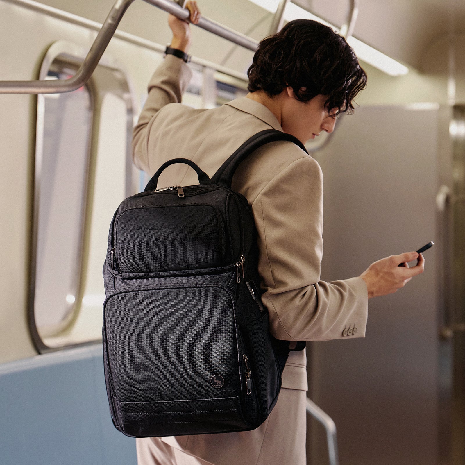 OIWAS laptop backpack in charcoal black, worn by a person commuting in urban setting, featuring USB charging port on side, padded shoulder straps, and front organizer pocket