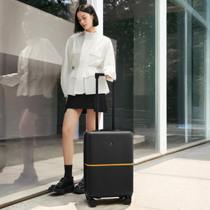 Woman holding a black suitcase with an orange stripe in front of a modern building — OIWAS Edge Collection