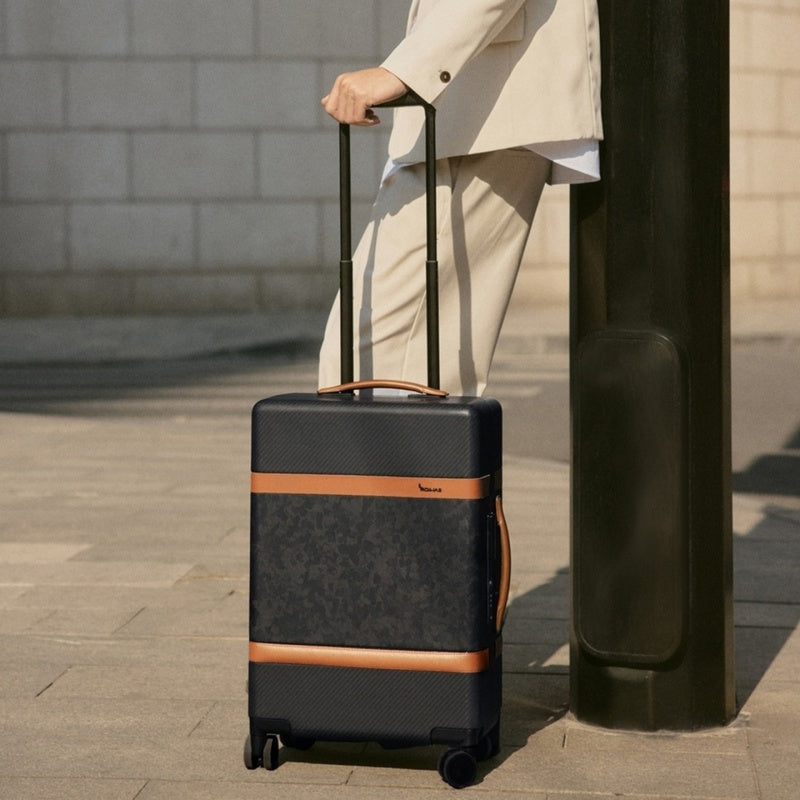 TIMELESS carbon fiber carry-on in urban travel setting: rolling through airport, fitting in overhead bin, and standing beside business attire.